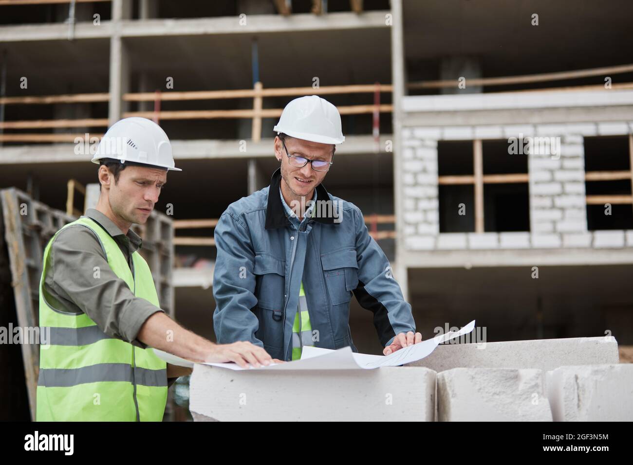 Waist up portrait of two workers discussing floor plans at construction site, copy space Stock Photo