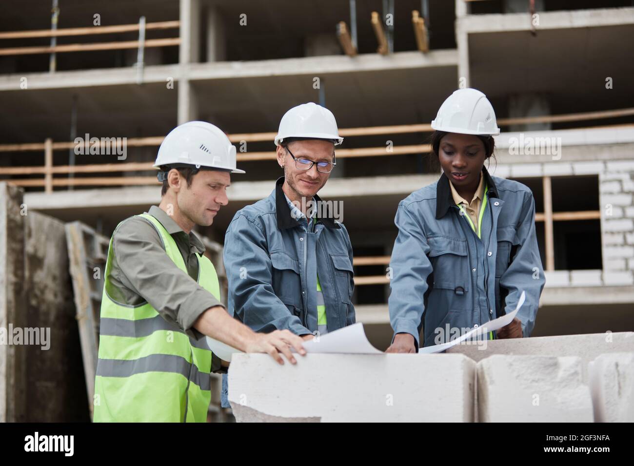 Waist up portrait of workers discussing floor plans at construction site, copy space Stock Photo