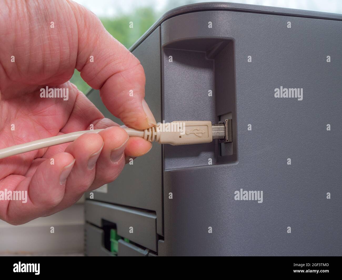 Closeup POV shot of a man’s hand plugging a cable / cord into the USB socket of a computer printer. Stock Photo