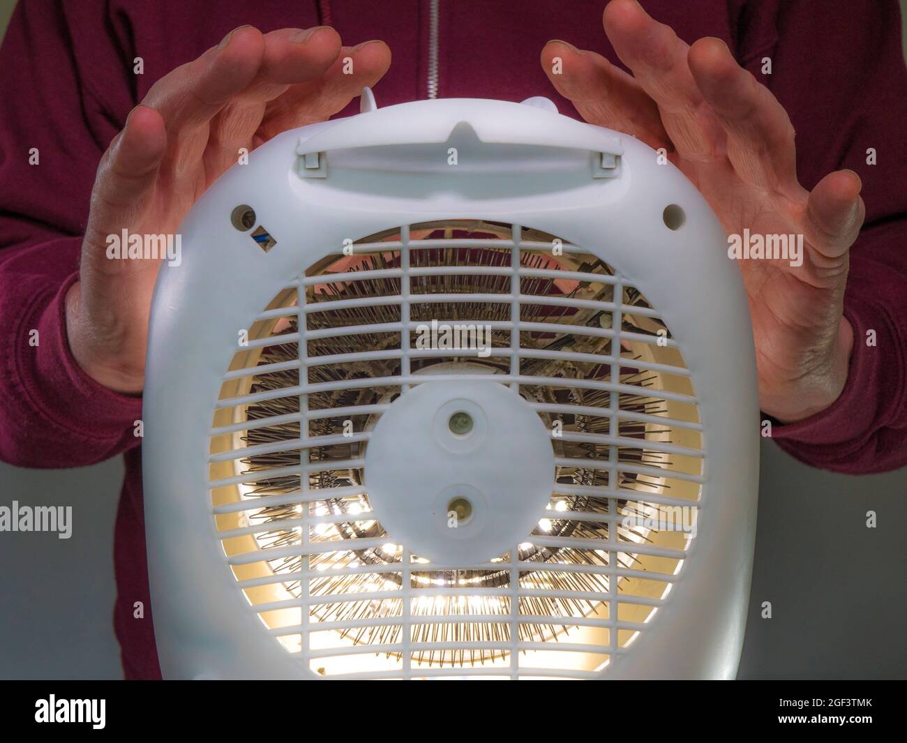 Closeup POV shot of a man warming his hands in front of a small, white,  plastic cased electric fan heater. Stock Photo
