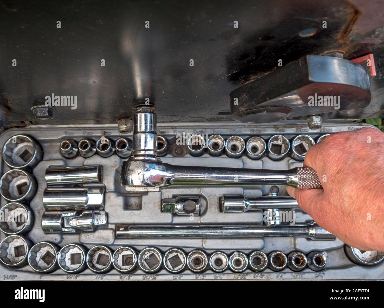 Closeup POV shot of a man’s hands using a chrome steel socket from the set below, attached to a ratchet, to loosen or tighten a machine bolt. Stock Photo
