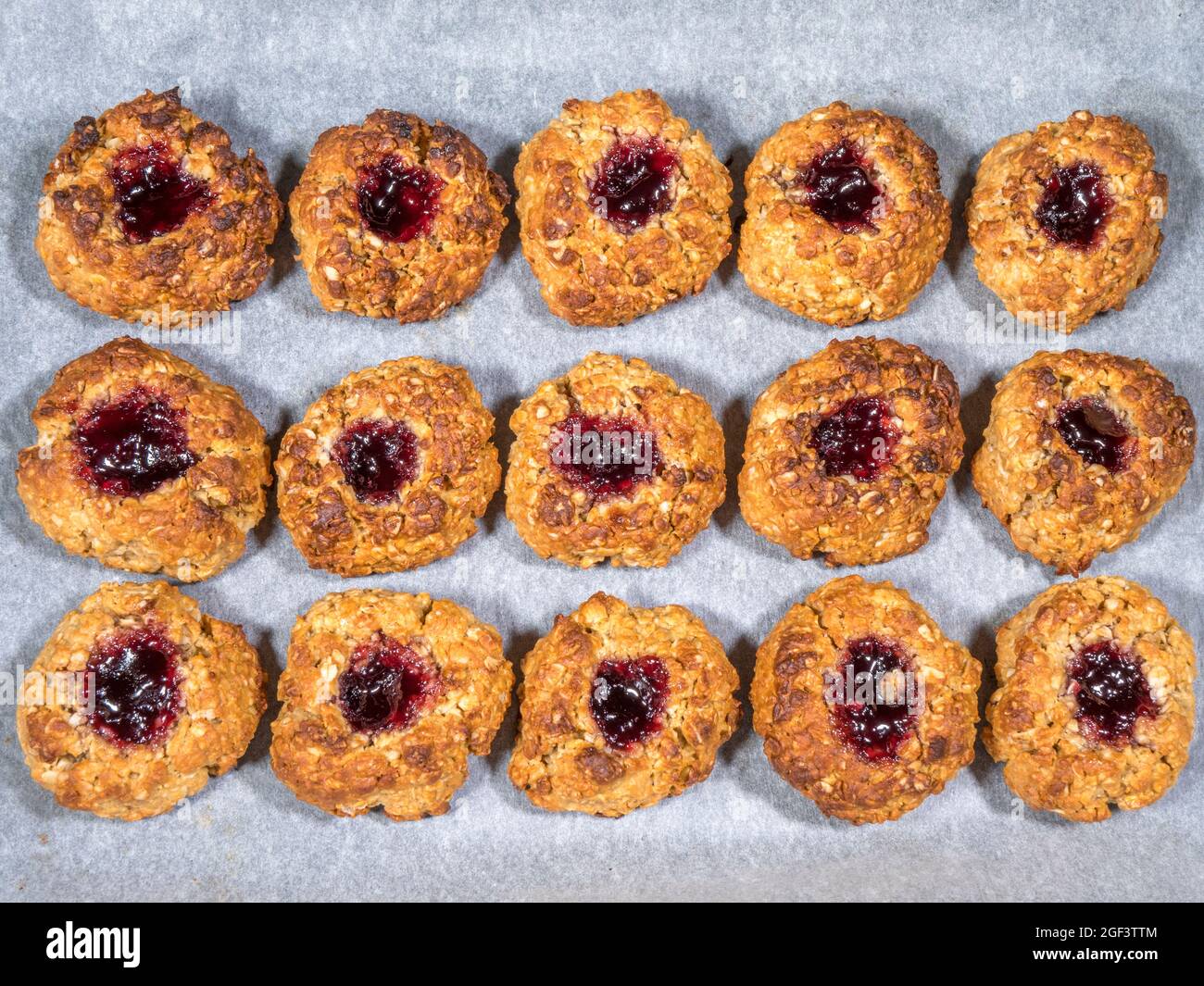 Closeup POV overhead shot of gluten free, peanut butter and jam oat cookies in rows on greaseproof paper. Stock Photo