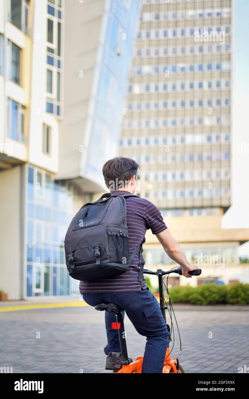 Young man with backpack, cyclist on a bicycle while biking around the city. The student riding to work or study by bike. Stock Photo