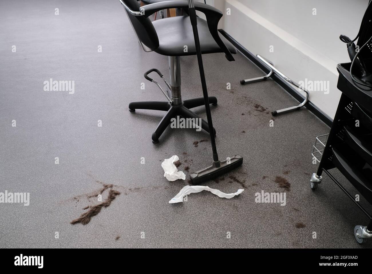 Hair on the floor after cutting hair in a barber shop. Hairdressers workspace with a rubber broom for cleaning hair from the floor. Stock Photo