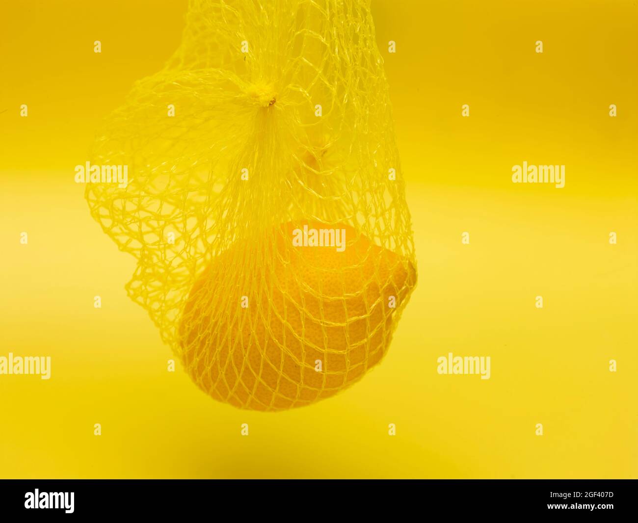 Lemon in string bag against yellow background in close-up. Food ...