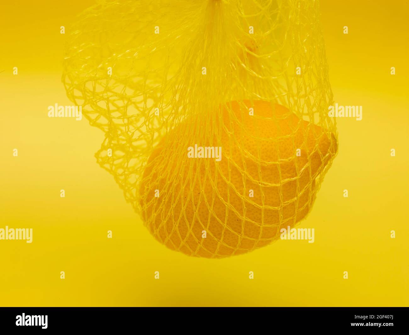 Lemon in string bag against yellow background in close-up. Food ...