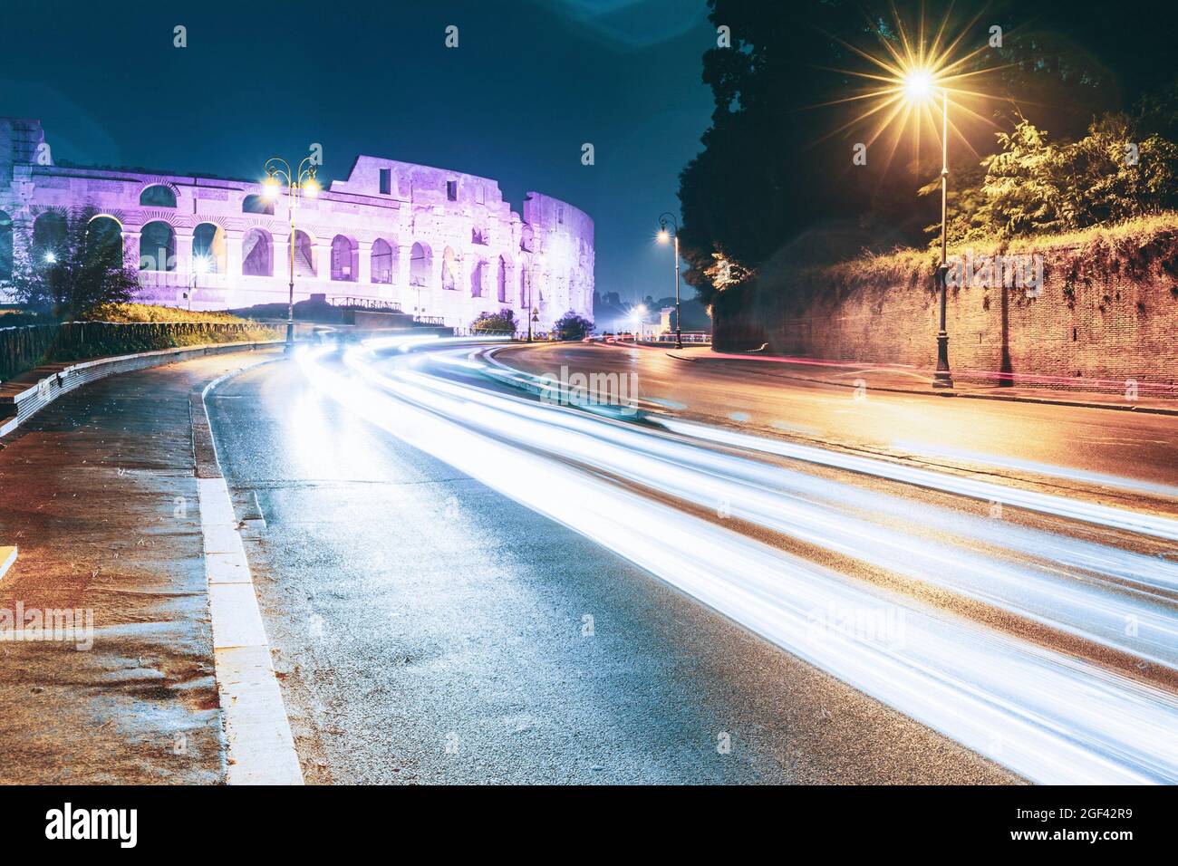 Rome, Italy. Colosseum View From Another Side In Night Time. Night Traffic Light Trails Near Famous World Landmark. Stock Photo