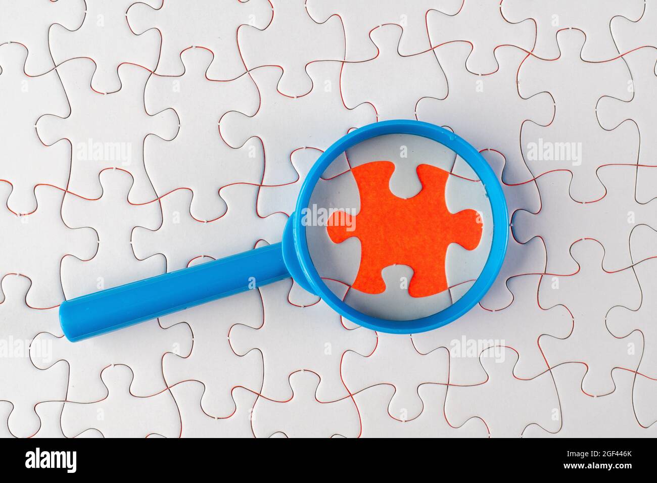 A magnifying glass on white jigsaw puzzle. Problem analysis and solving