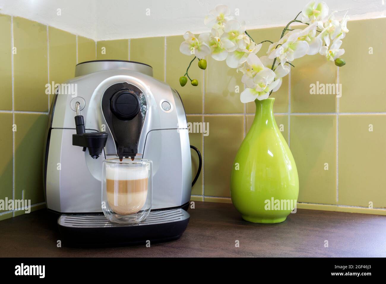 Coffee machine maker with a latte macchiato in cozy decorative home with green wall and flowers. home made coffee stylish. Stock Photo