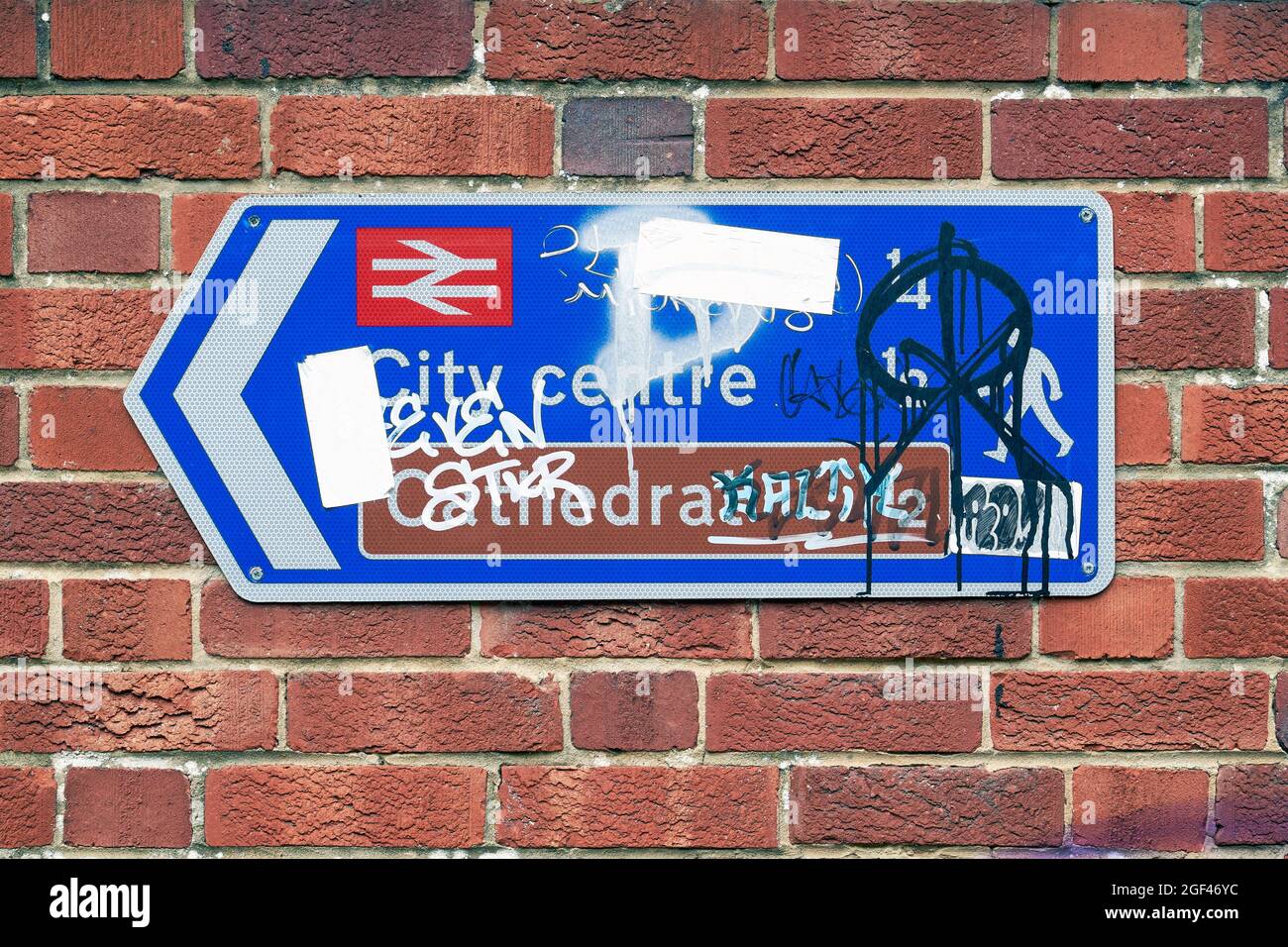 Graffiti covered and vandalised direction sign on red brick wall Stock Photo