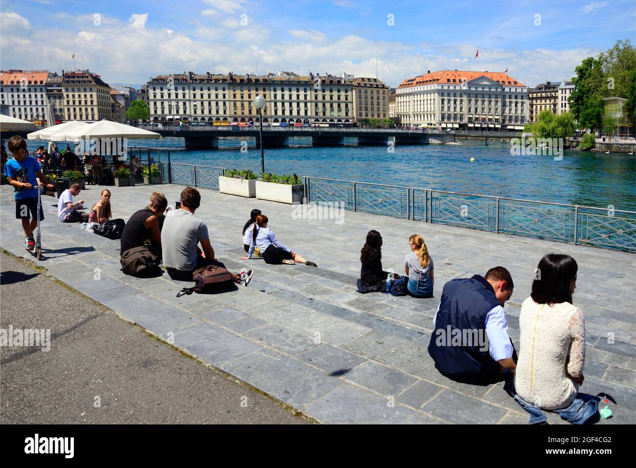 People resting on terraces on bank of Rhone river, Promenade du Lac, on lef Pont des Bergues( Bergues bridge) connecting banks of river, on right Île Stock Photo