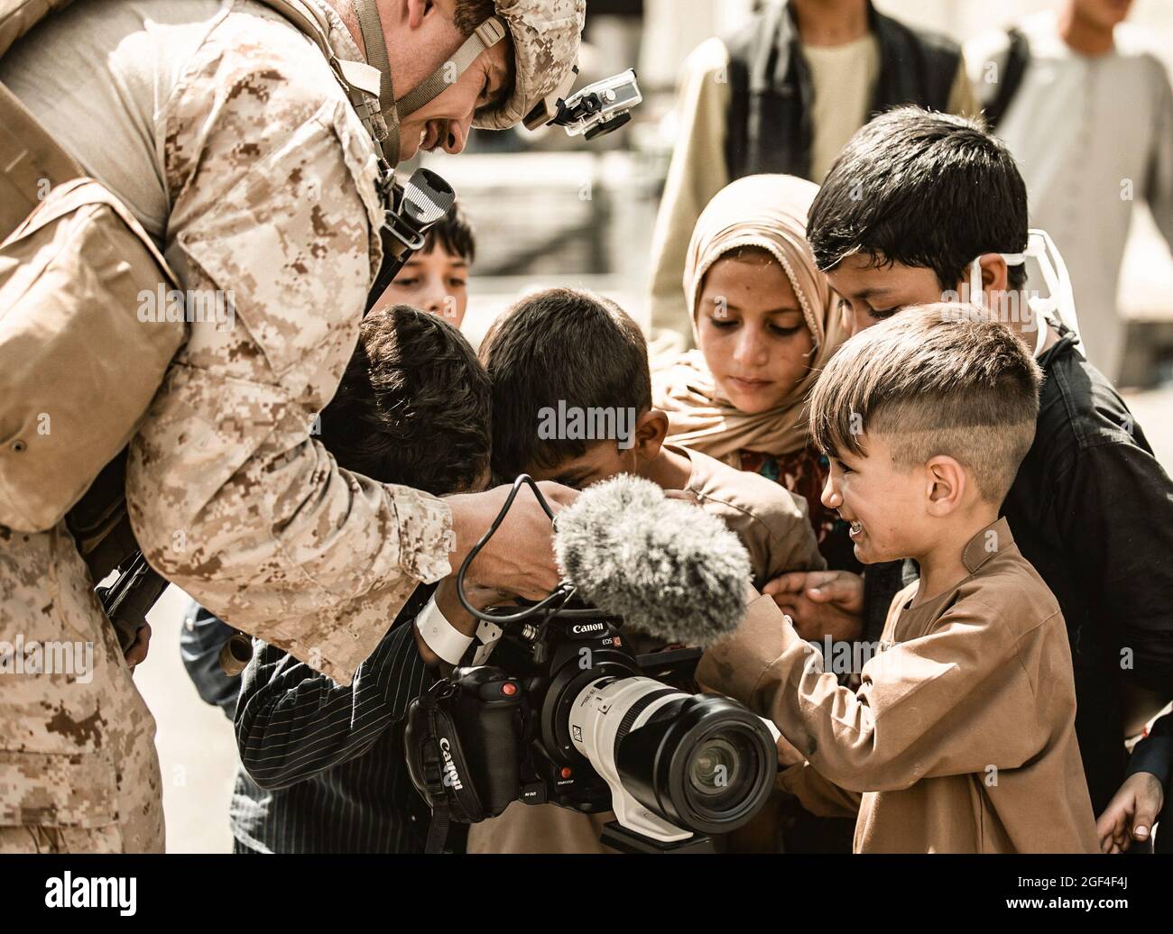 A U.S. Marine assigned to Special Purpose Marine Air-Ground Task Force – Crisis Response – Central Command shows his video camera to children awaiting evacuation at Hamid Karzai International Airport, Afghanistan, Aug. 22, 2021. The U.S. is assisting the Department of State with a Non-Combatant Evacuation Operation (NEO) in Afghanistan. (U.S. Marine Corps photo by Gunnery Sgt. Melissa Marnell) Stock Photo