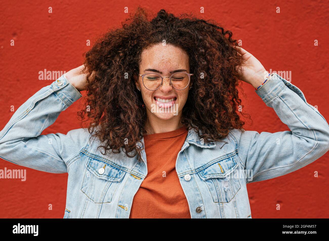 Playful woman sticking out tongue with hands in curly hair Stock Photo
