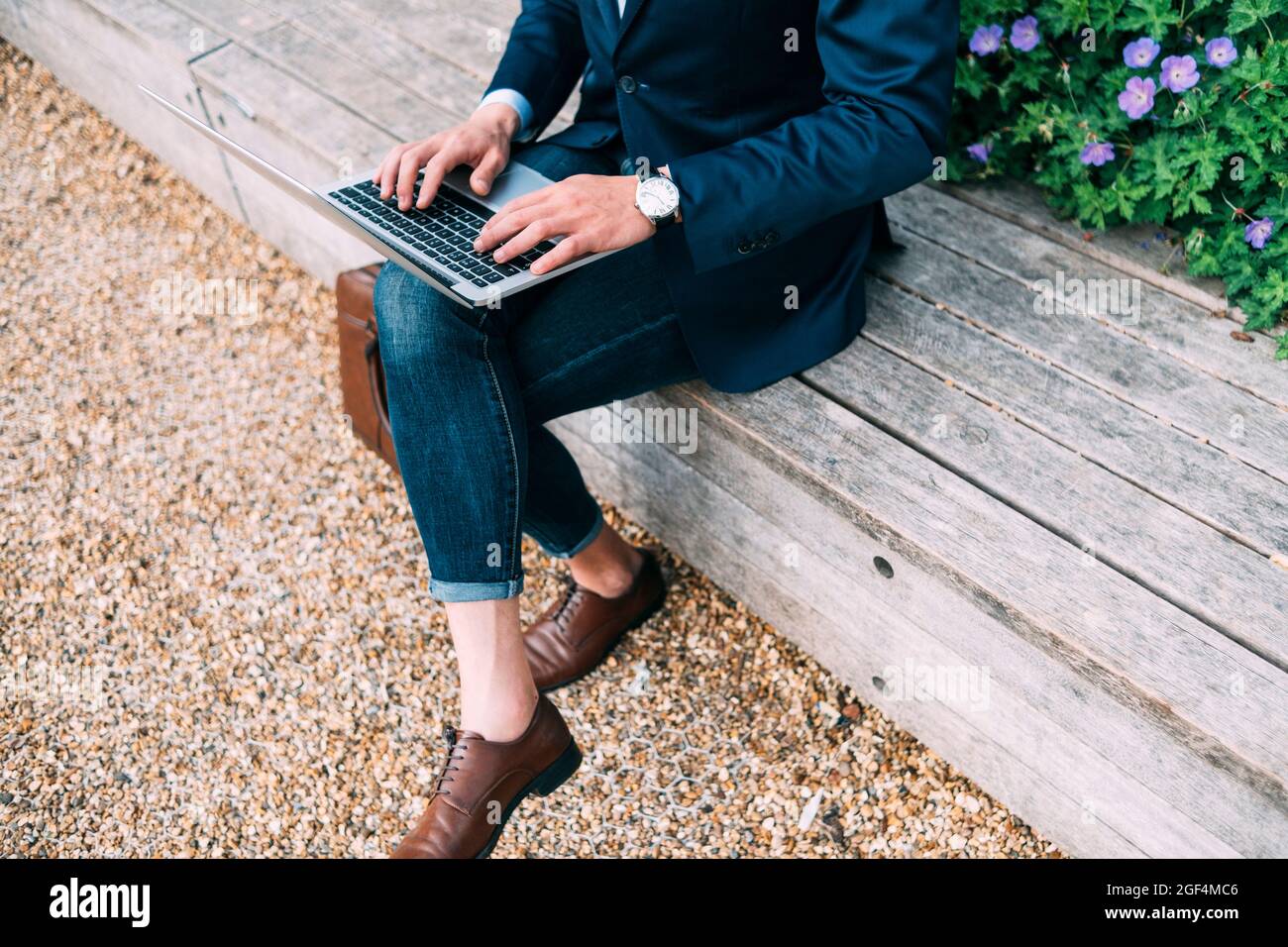 Businessman using laptop while sitting with legs crossed at knee on bench Stock Photo