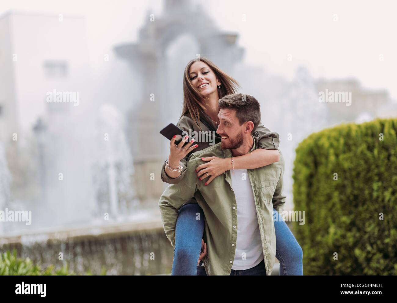 Smiling woman using mobile phone while piggybacking on boyfriend Stock Photo