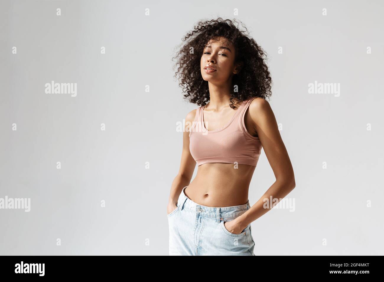 Beautiful black woman with an afro hairstyle wear white bra and blue jeans  looking at camera and smiling Stock Photo