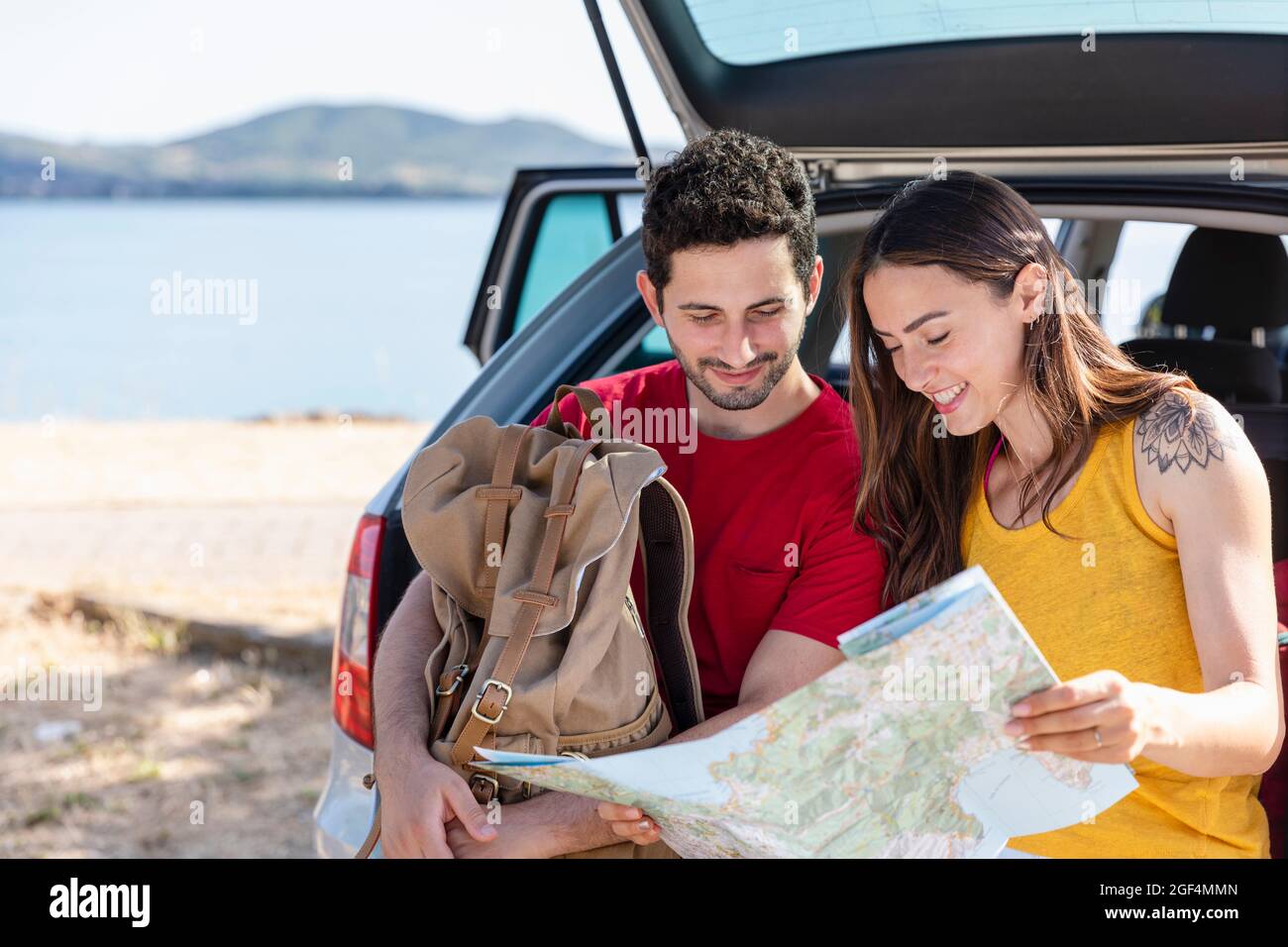 Boyfriend holding backpack while checking map with girlfriend during road trip Stock Photo