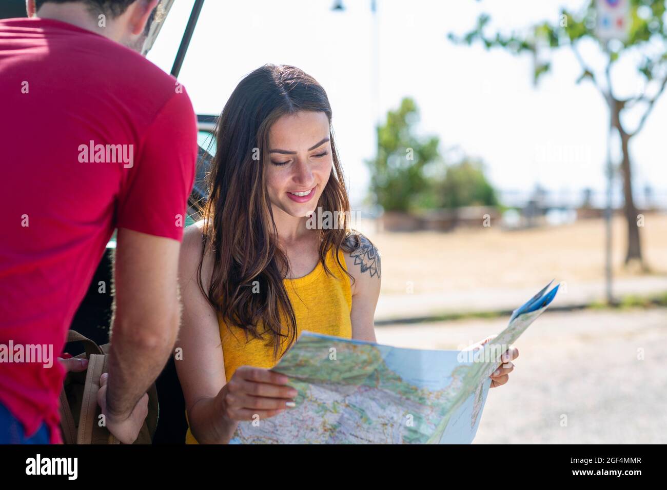Smiling woman holding map while sitting by man in car trunk Stock Photo