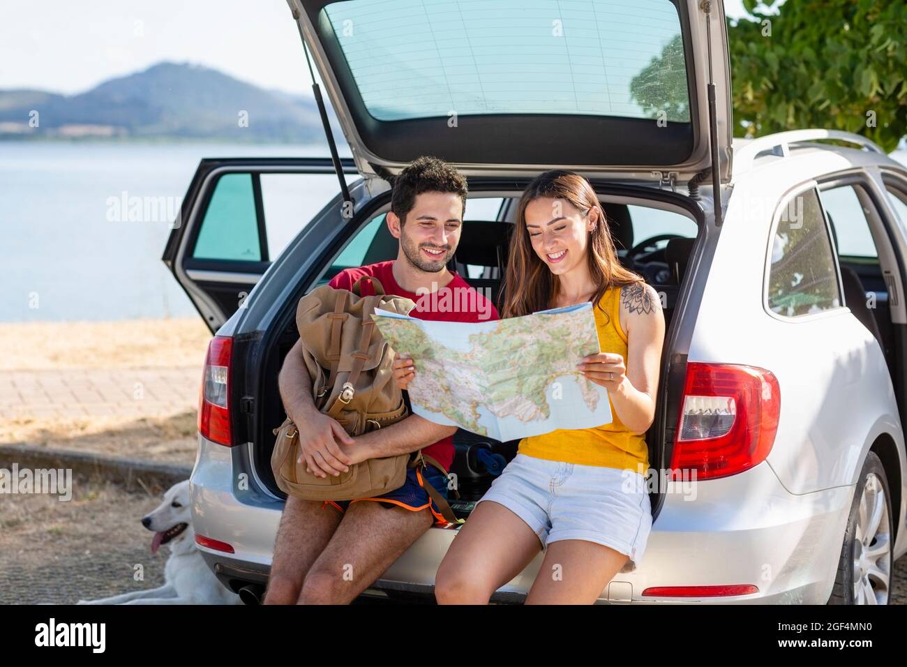 Smiling couple checking map while sitting in car trunk Stock Photo