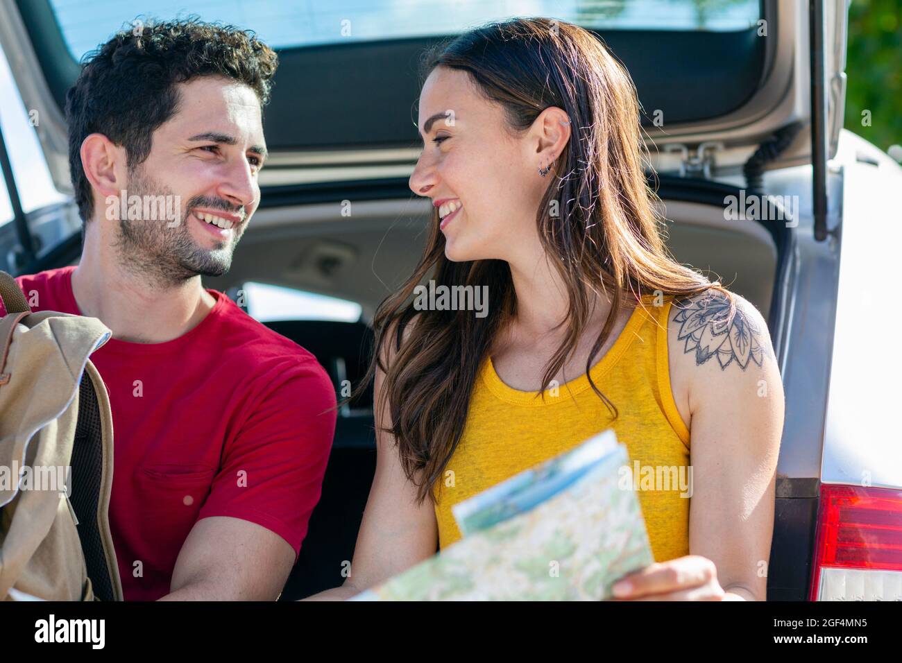 Smiling girlfriend looking at boyfriend while sitting in car trunk Stock Photo
