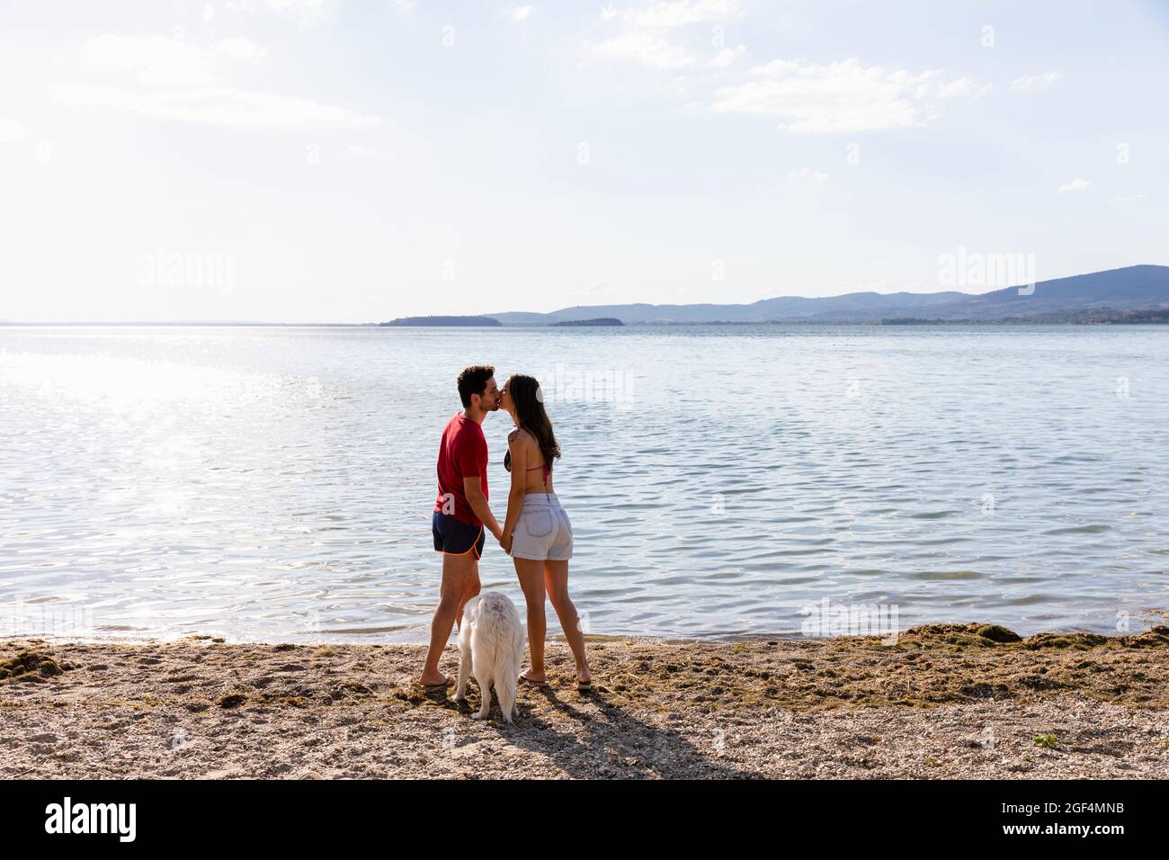 Couple kissing each other while standing by pet at lakeshore Stock Photo