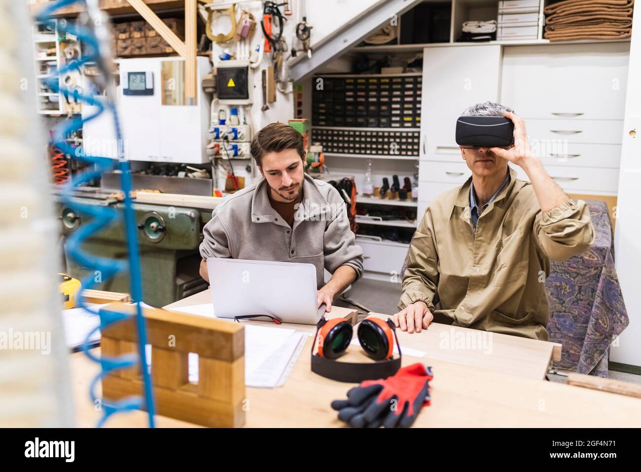 Male carpenter using virtual reality simulator while coworker using laptop in workshop Stock Photo
