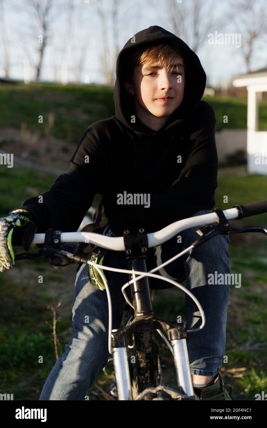 Teenage boy in black hoodie sitting on bicycle at backyard Stock Photo