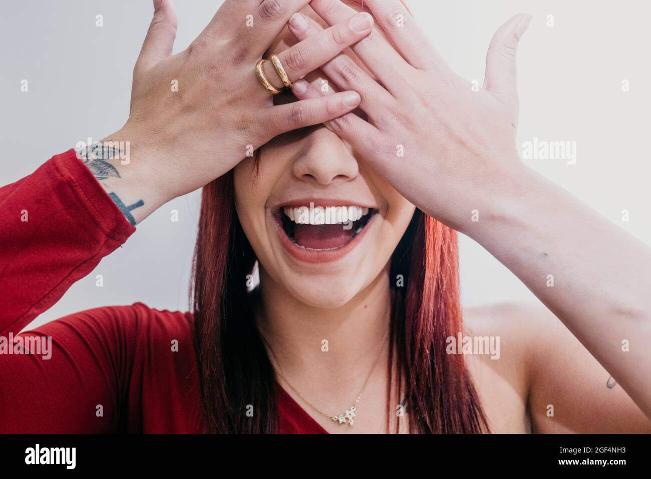 Happy woman covering eyes with hands in front of white background Stock Photo