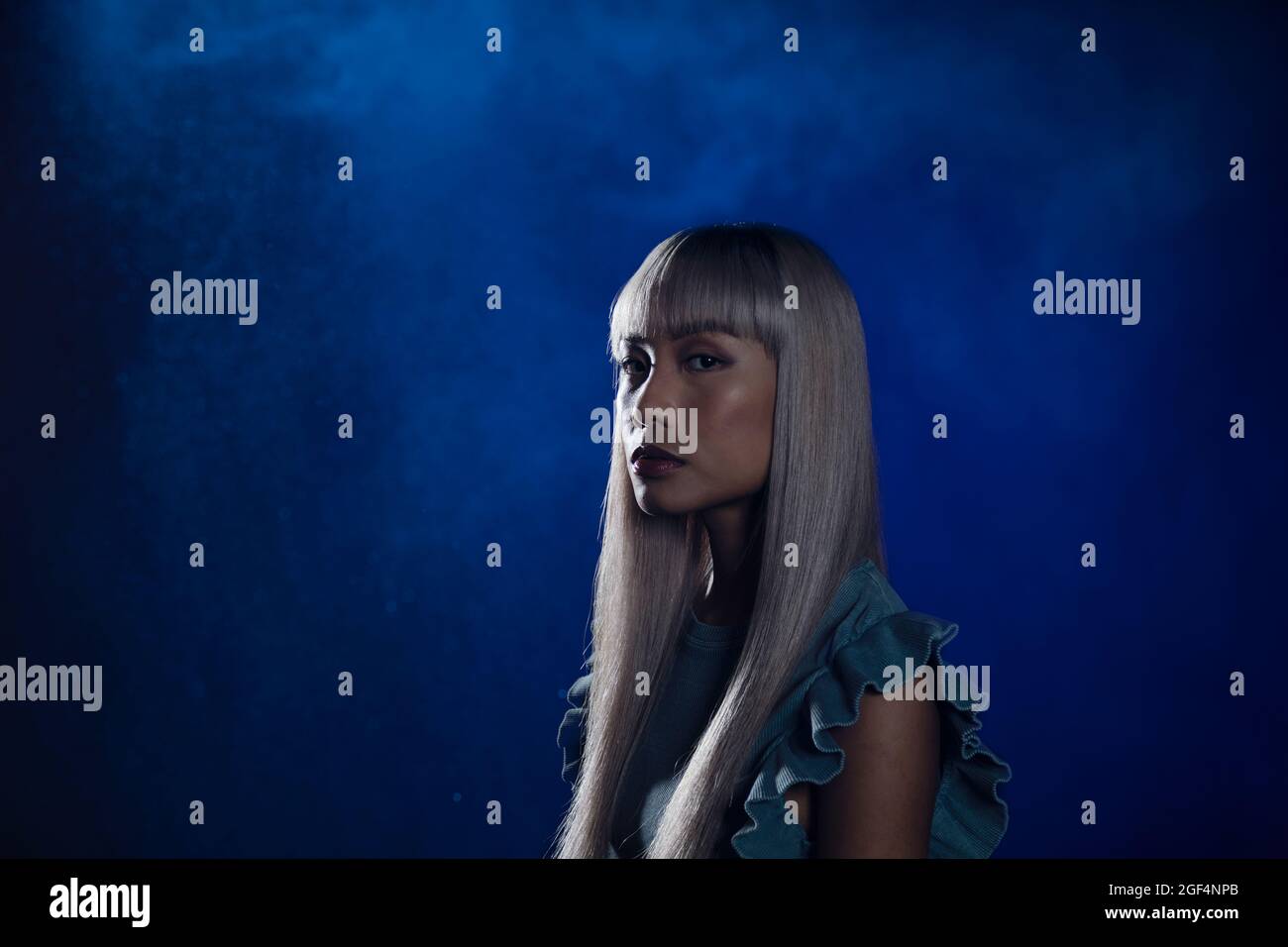 Woman with bangs staring against blue background Stock Photo