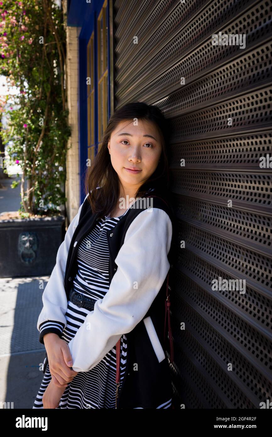 Portrait of a beautiful young asian woman leaning on roll up metal security door in San Francisco Stock Photo