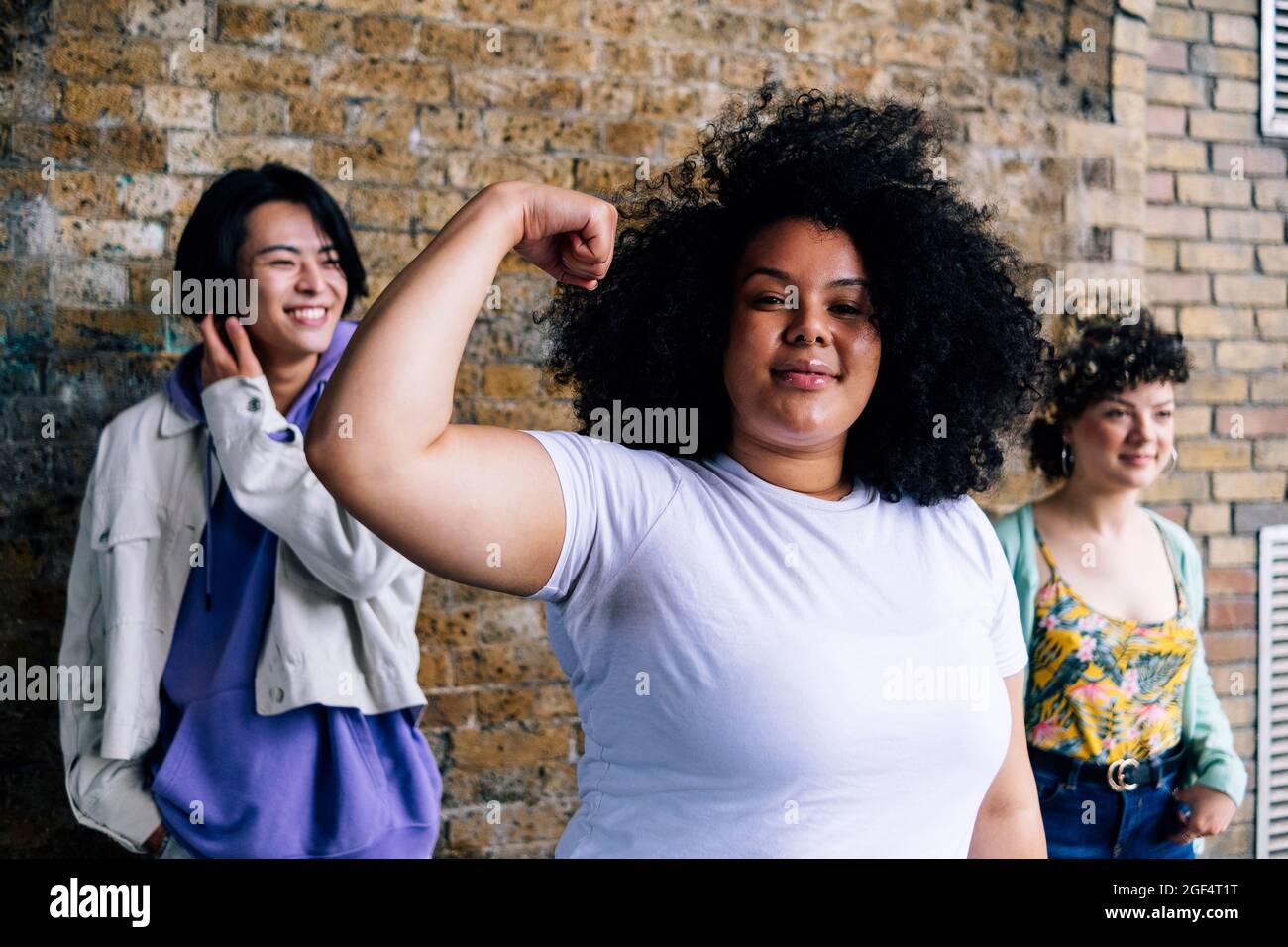 Young woman flexing muscle with male and female friends in background Stock Photo