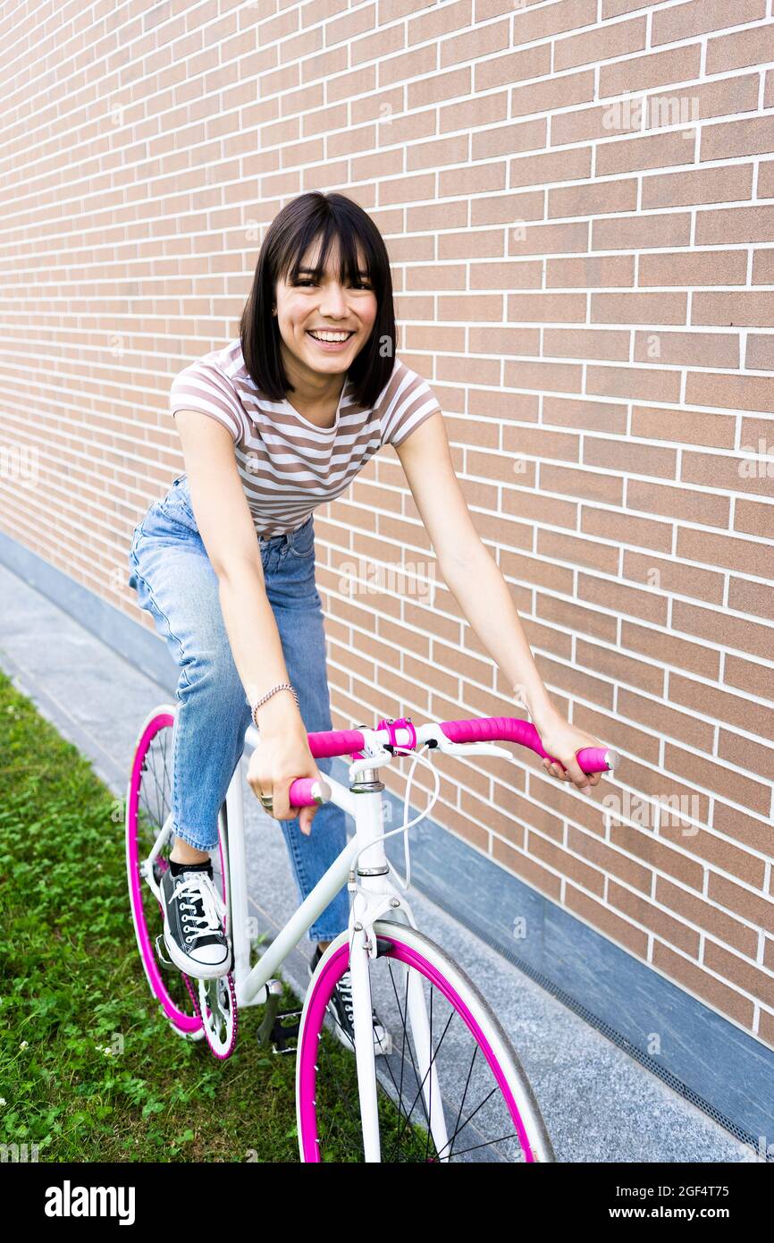 Beautiful woman cycling by wall Stock Photo