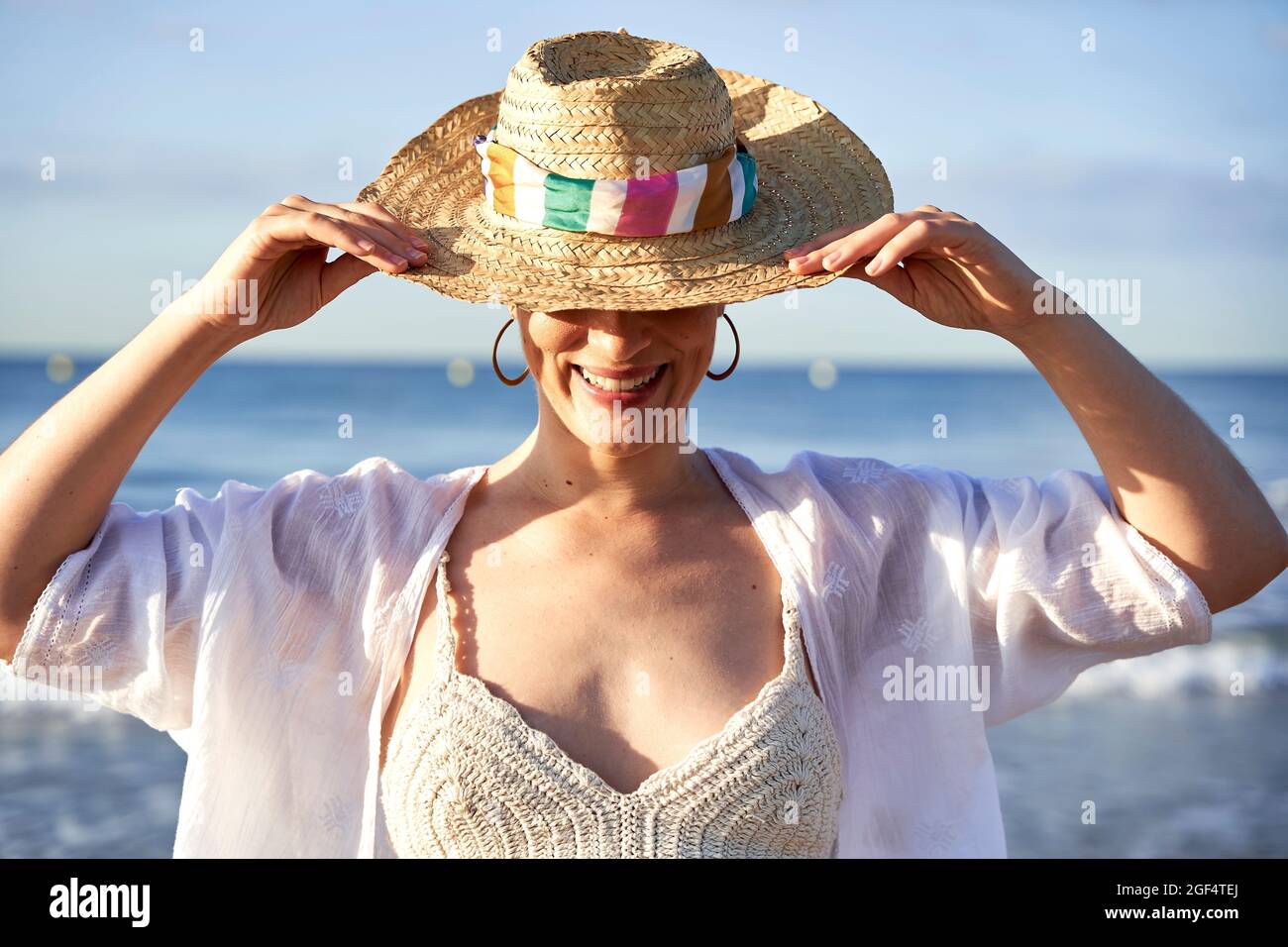 Woman smiling while holding hat at beach Stock Photo - Alamy