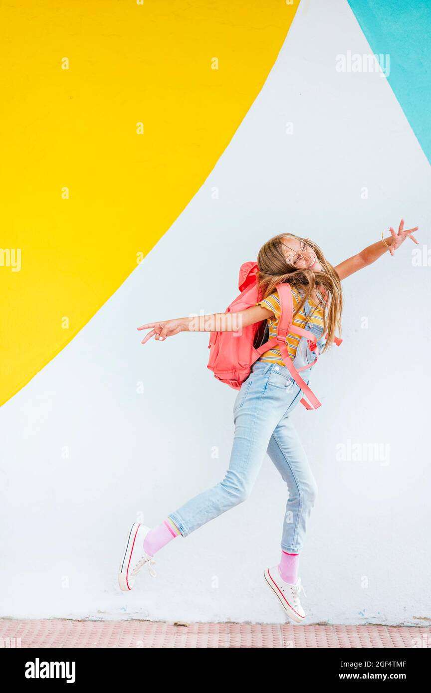 Smiling girl carrying backpack while standing in front of wall Stock ...