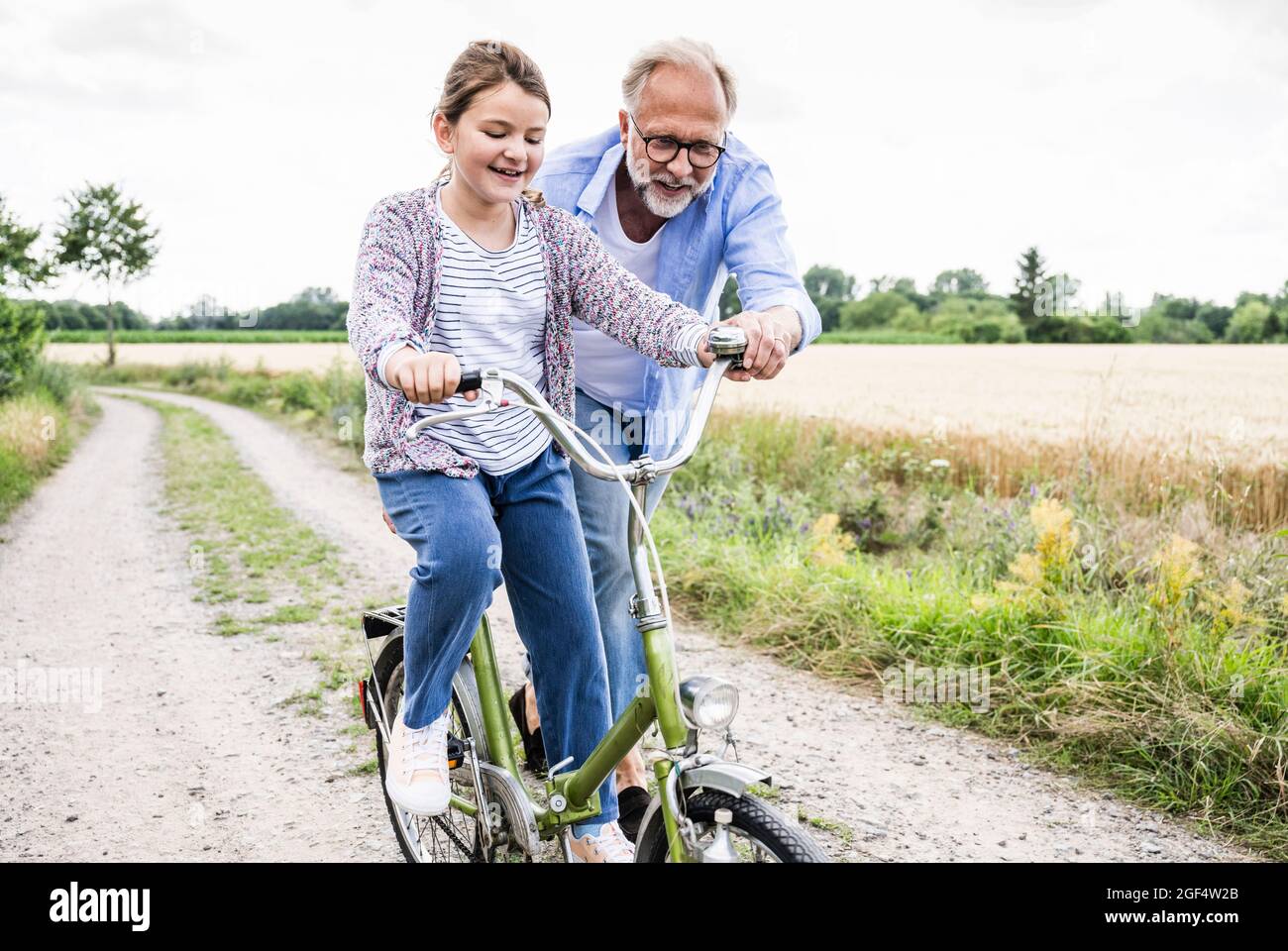 Grandfather teaching cycling to granddaughter on dirt road Stock Photo