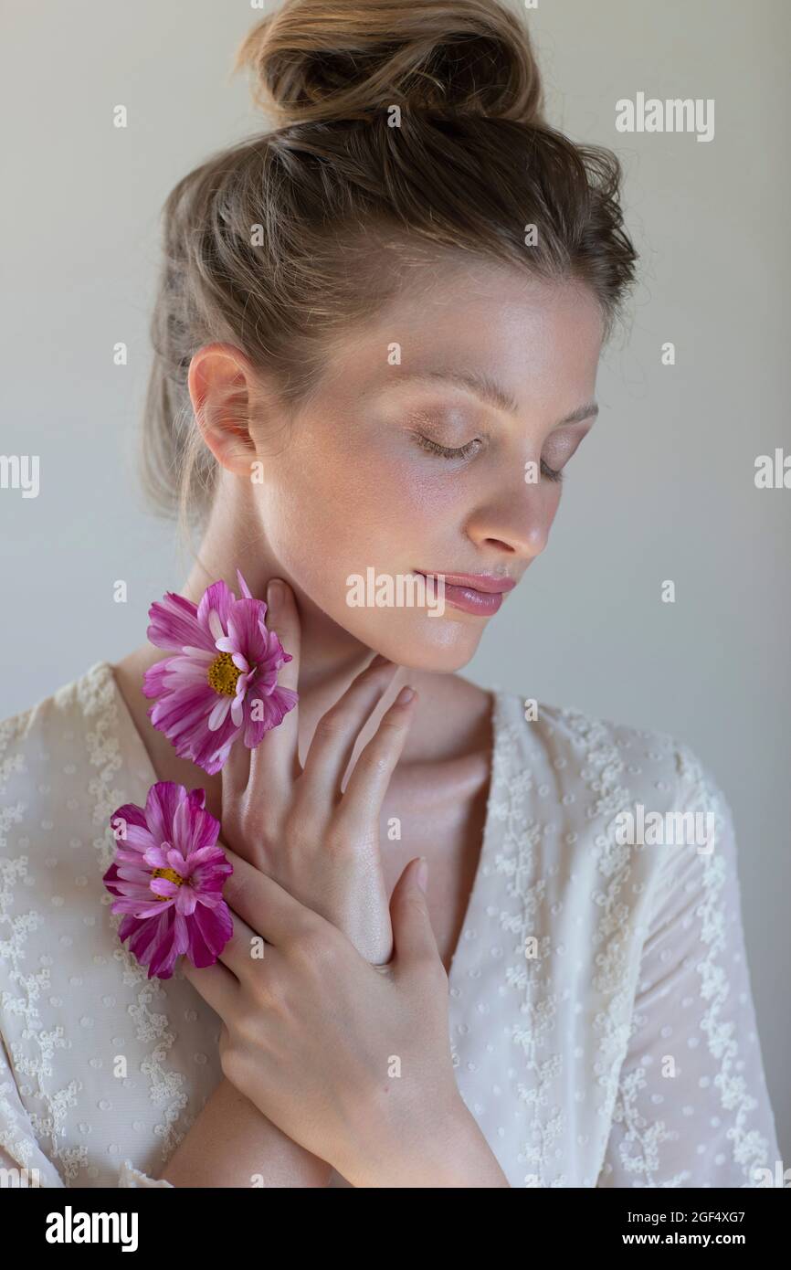 Young beautiful woman with eyes closed holding purple daisy in front of ...