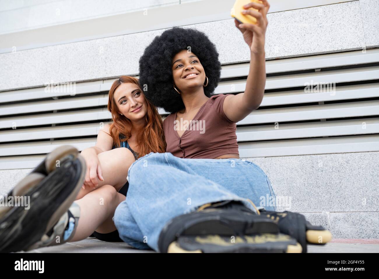 Smiling Afro woman taking selfie with female friend in front of wall ...