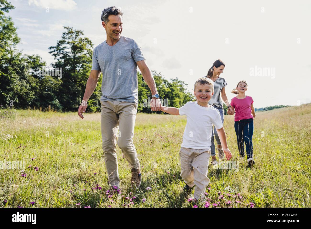 Parents holding hands of children while walking on grass Stock Photo