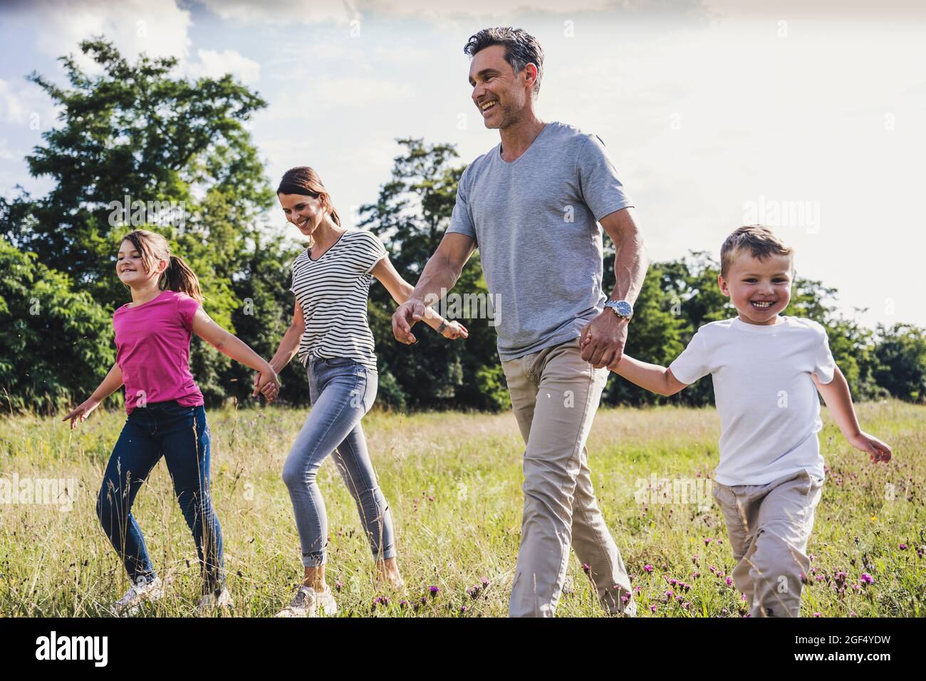Smiling family holding hands while walking on grass Stock Photo