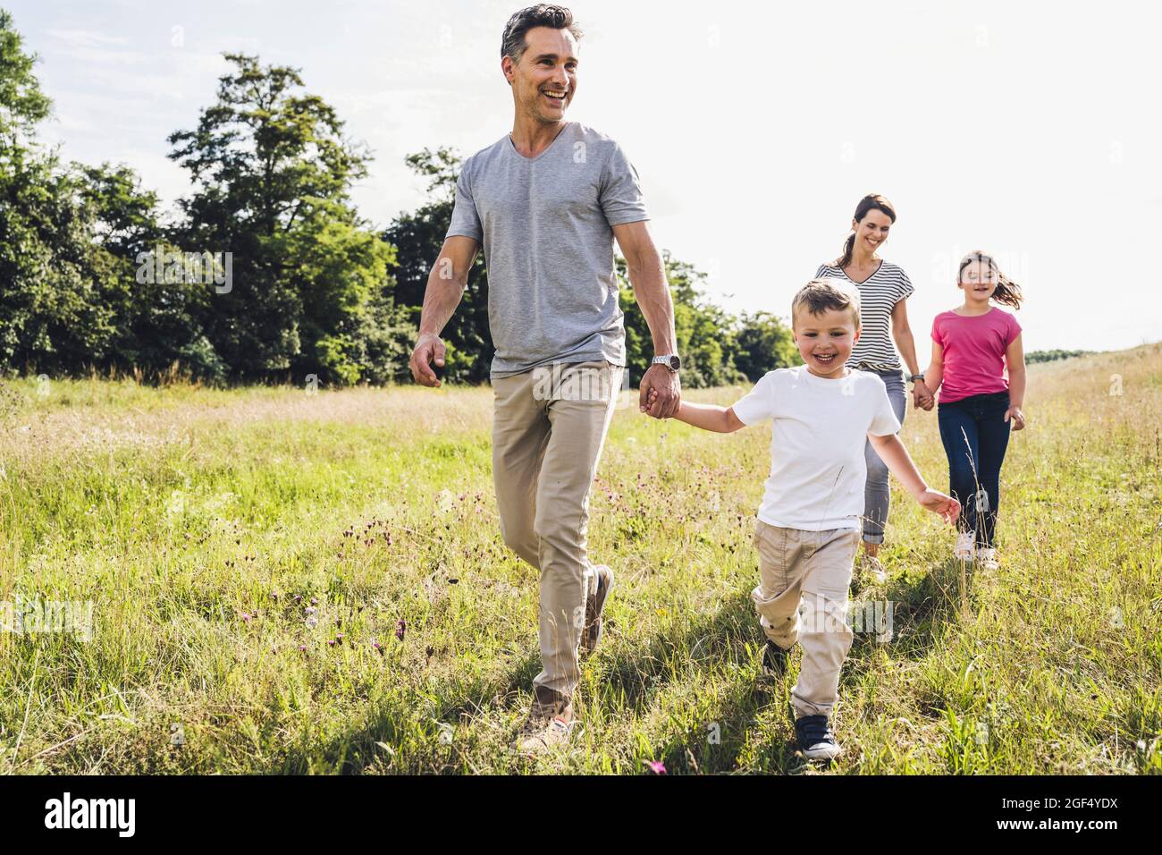 Parents holding hands of children while walking on grass during sunny day Stock Photo
