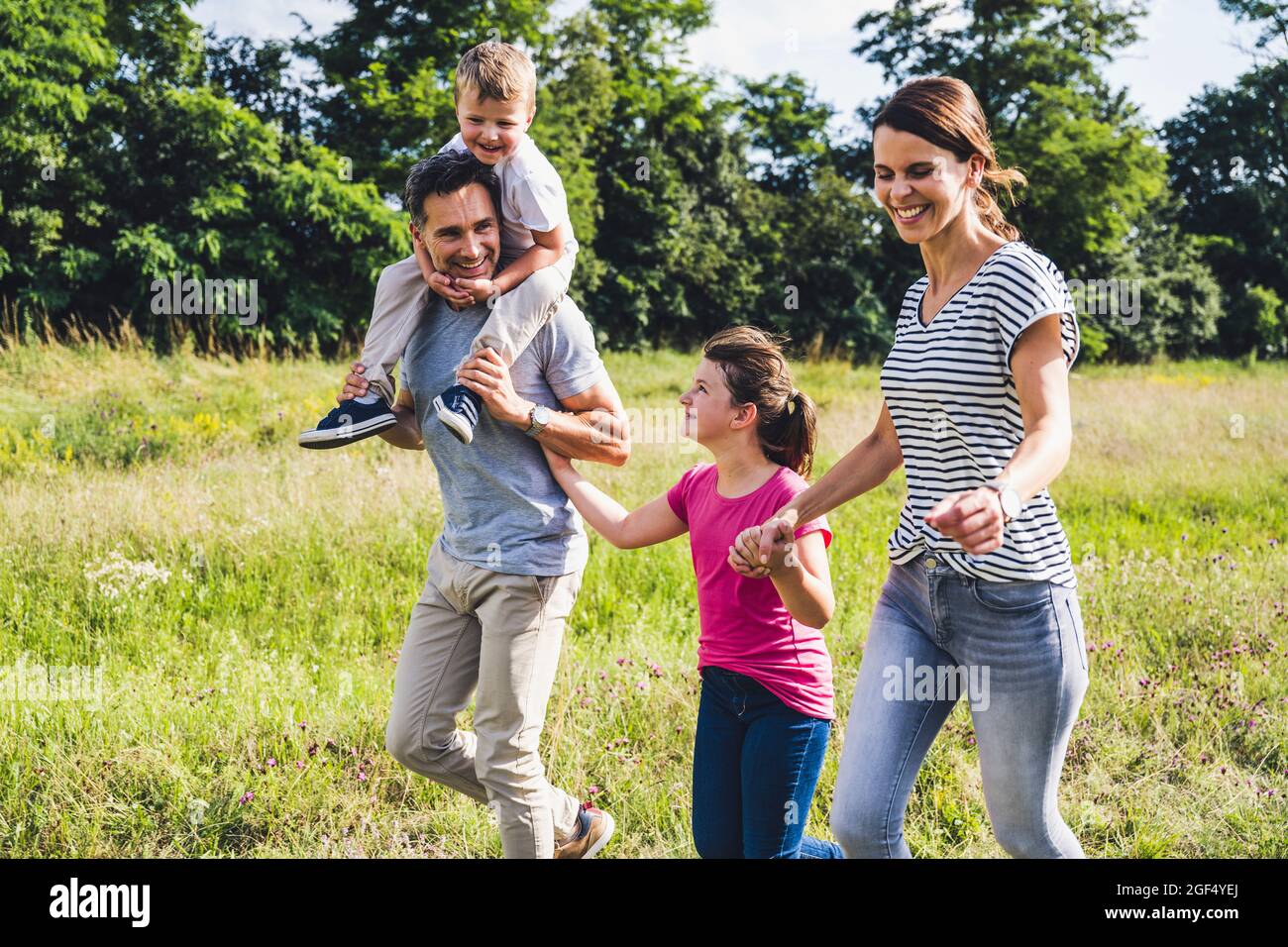 Father carrying son on shoulders while walking with family at meadow Stock Photo