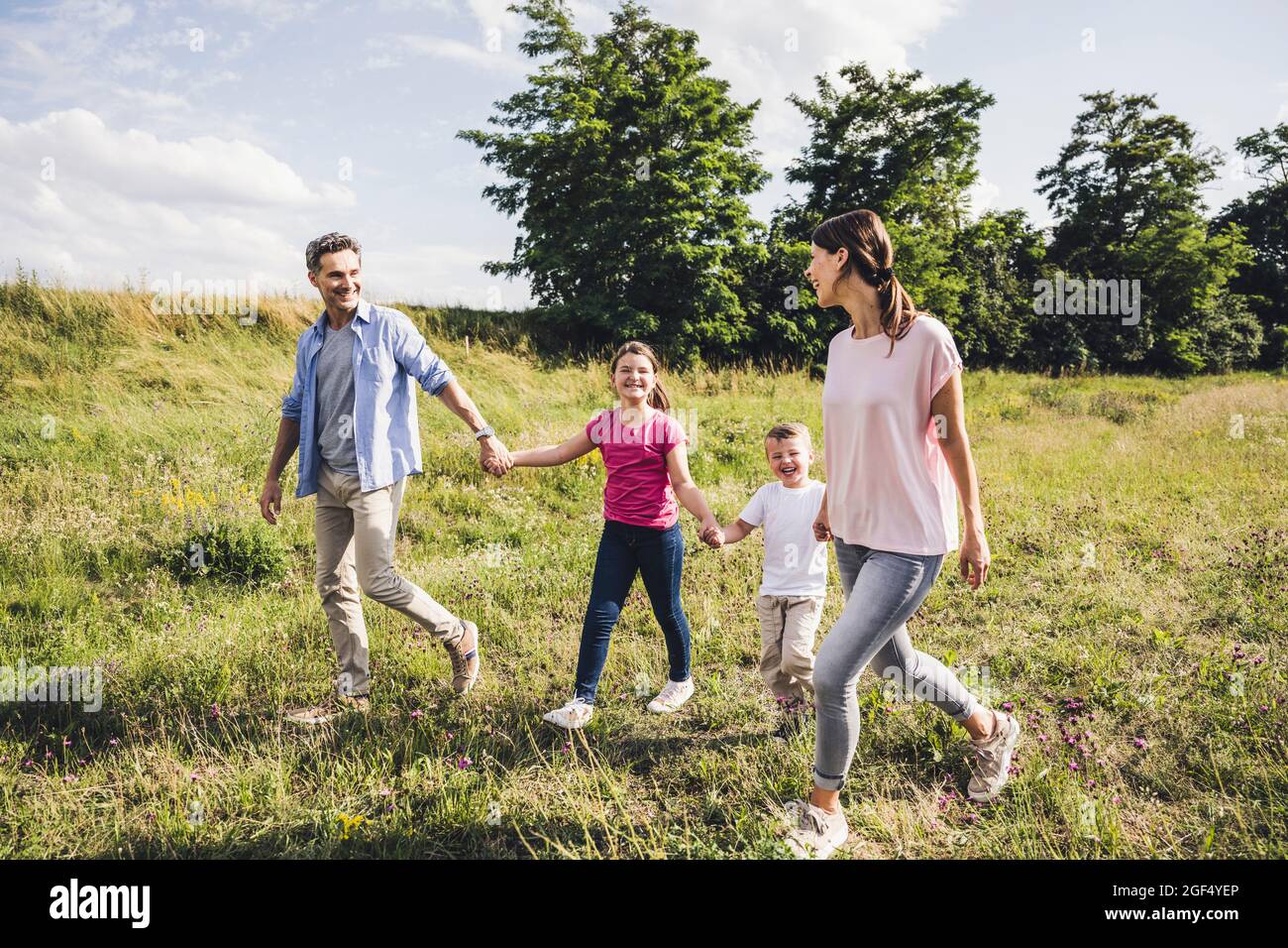Smiling family holding hands while walking on grass Stock Photo