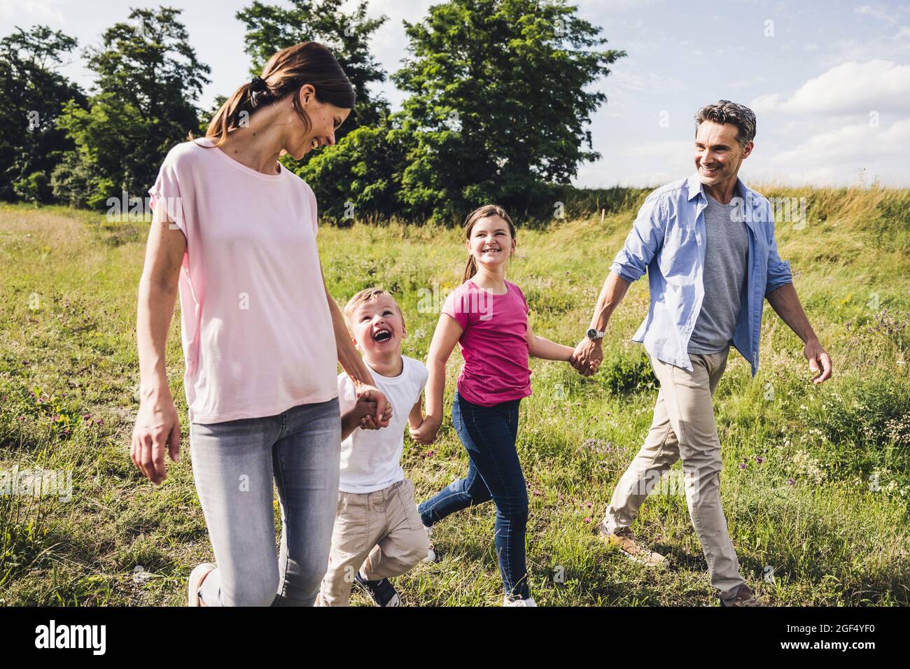 Children holding hands of parents while walking at meadow Stock Photo