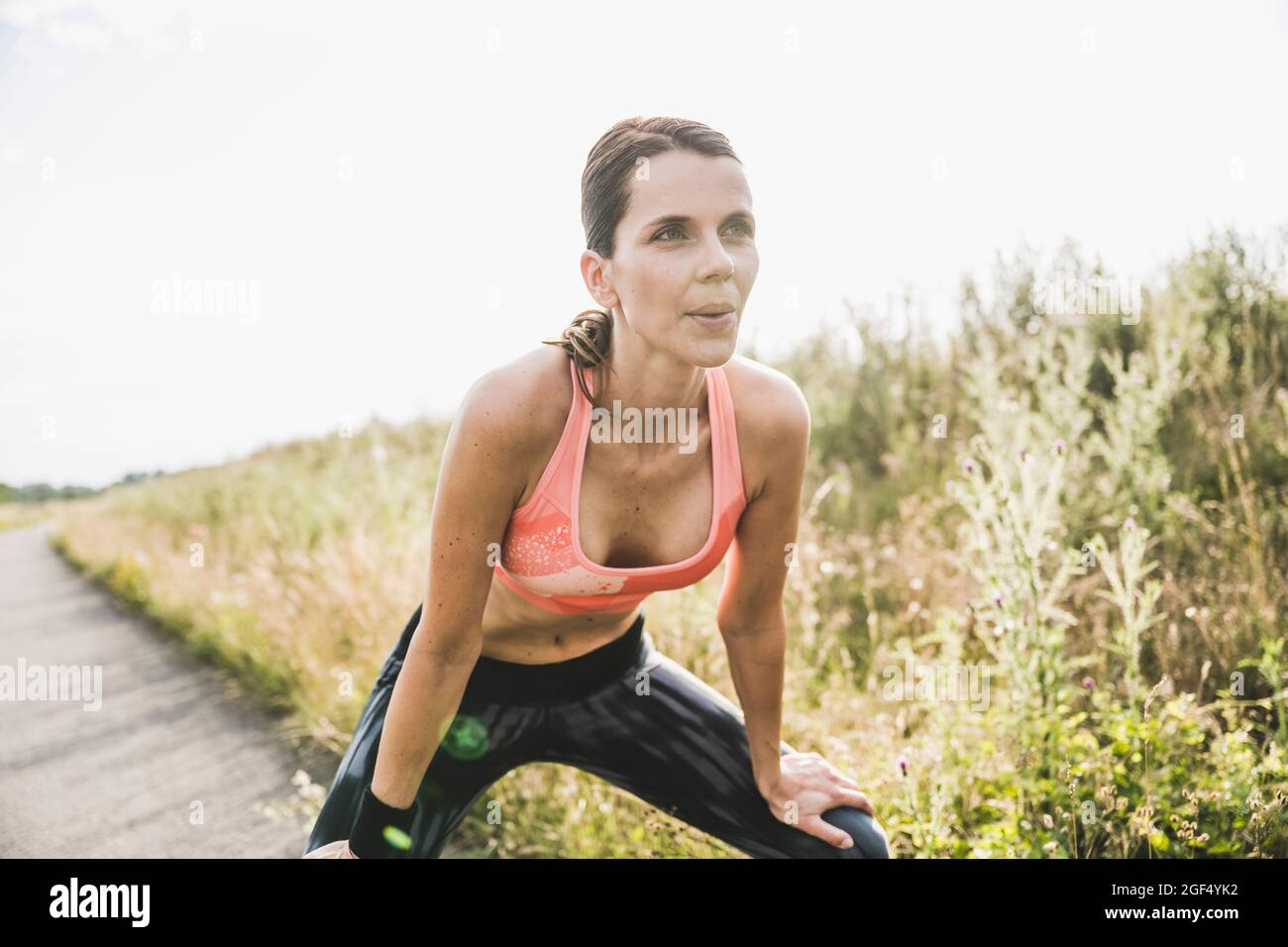 Exhausted sportswoman breathing while bending over on road Stock Photo