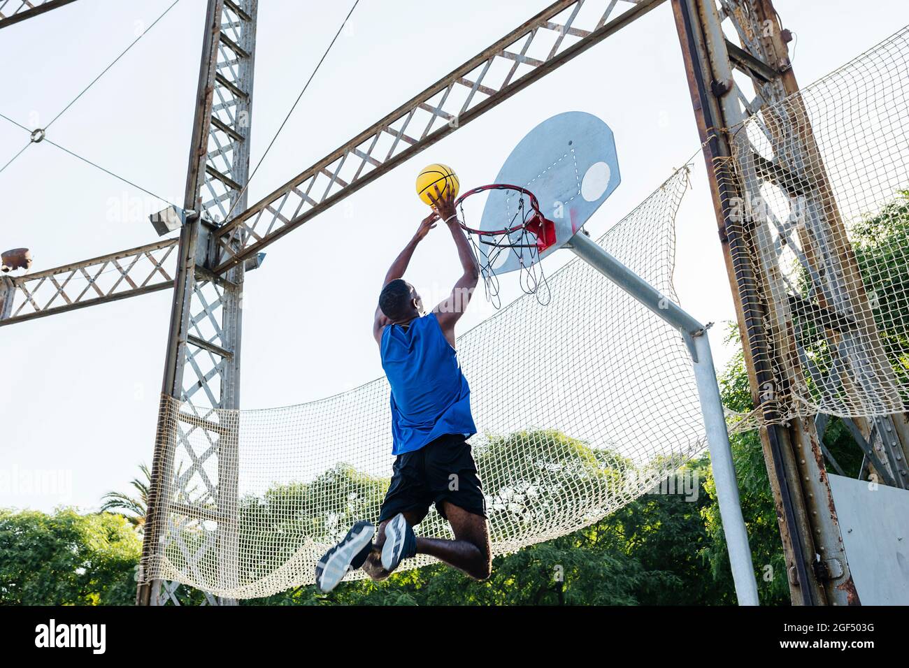 Young man dunking basketball while playing at sports court Stock Photo