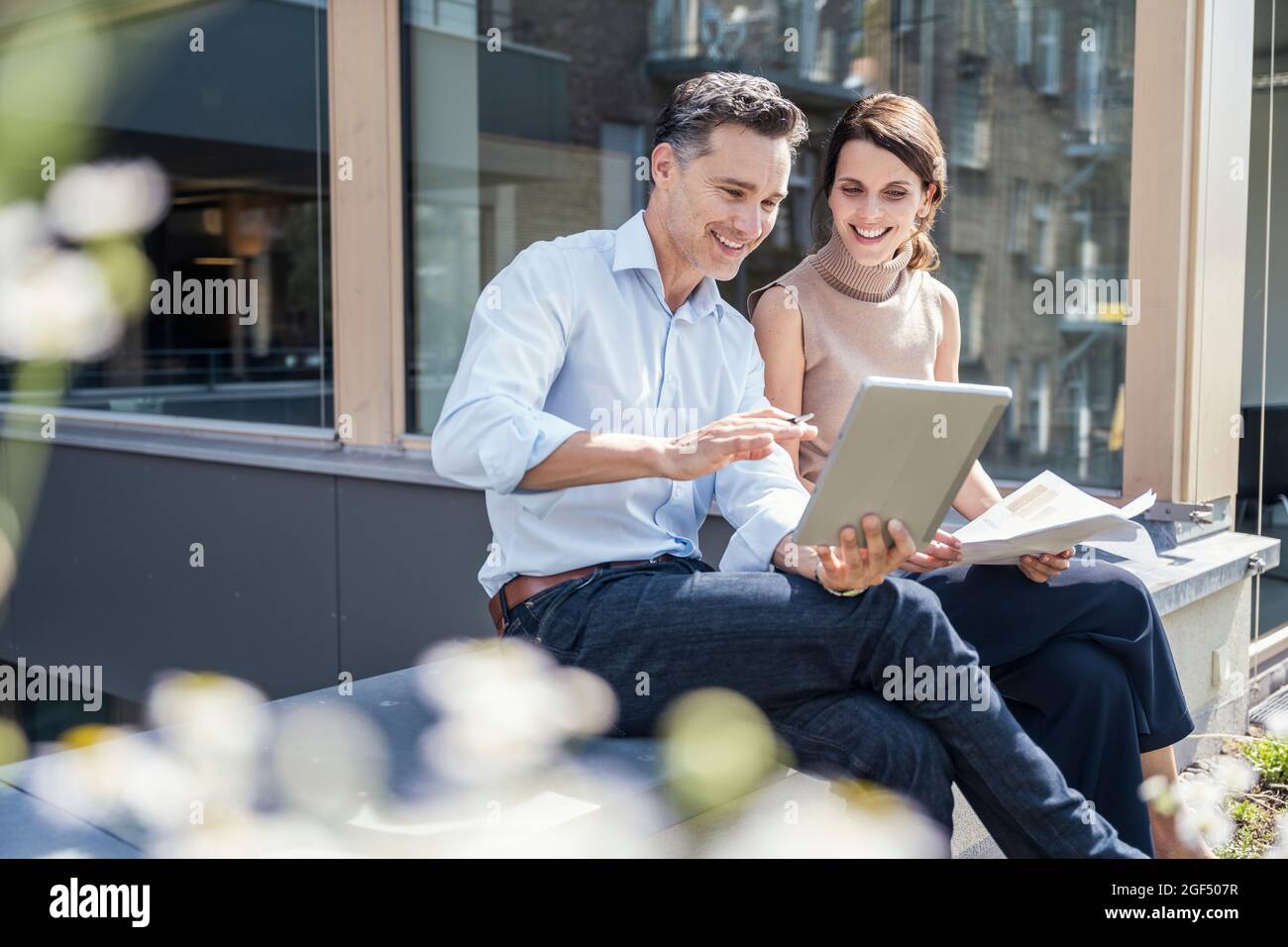 Smiling partners discussing while using digital tablet Stock Photo