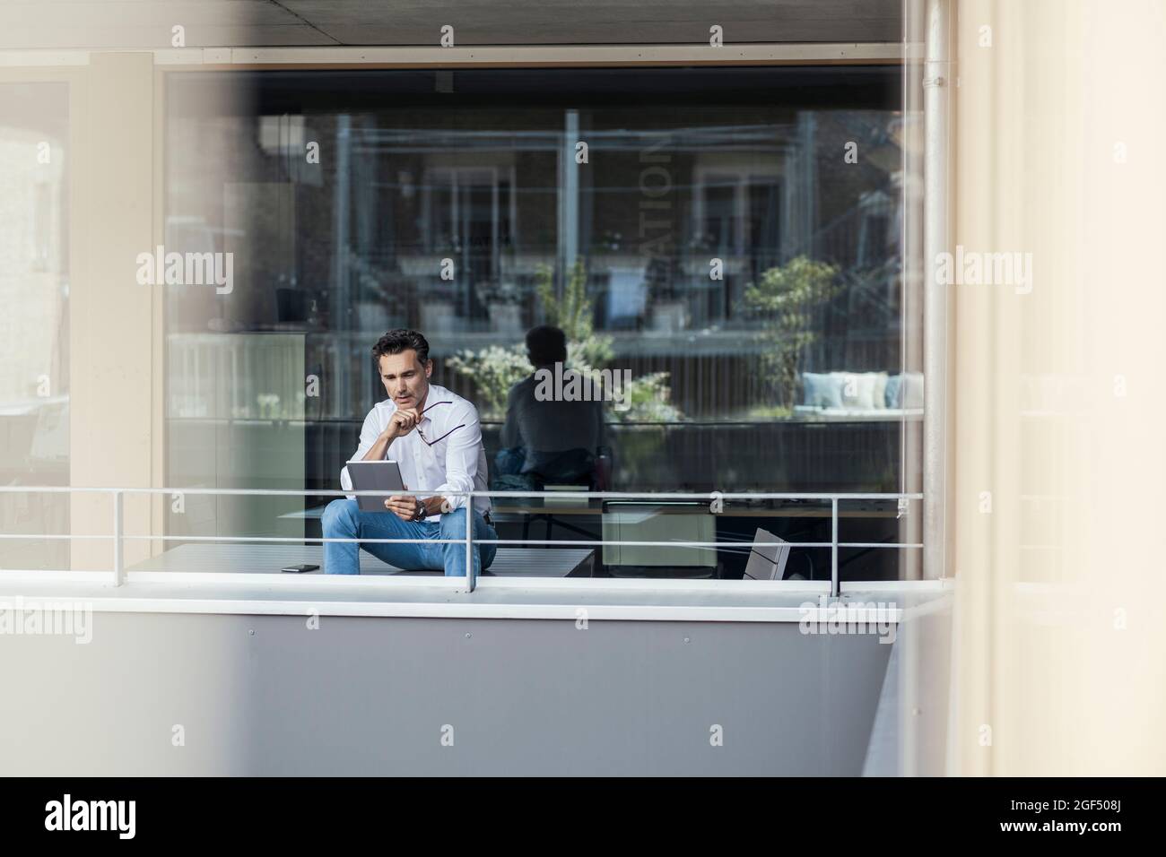 Thoughtful businessman using digital tablet while sitting at office balcony Stock Photo