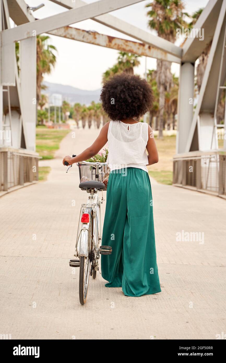 Afro woman with bicycle walking on bridge Stock Photo