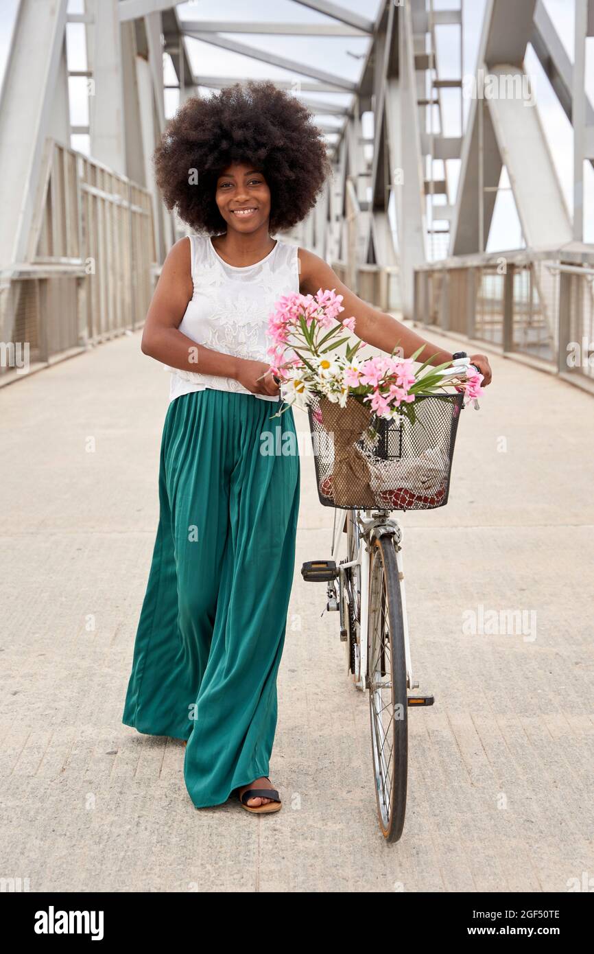 Afro woman walking with bicycle on bridge Stock Photo