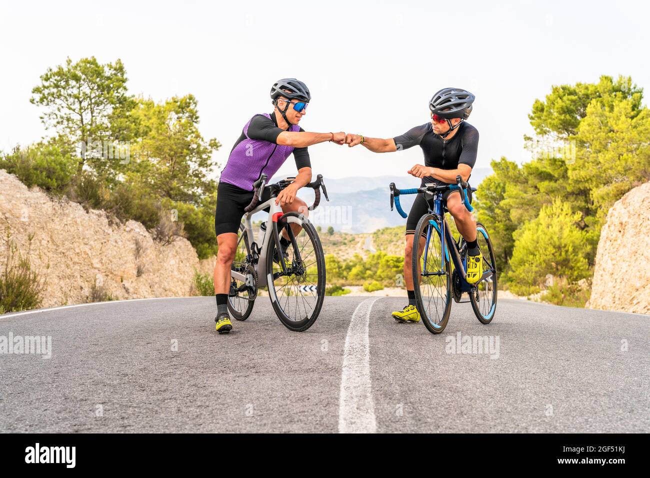 Male athletes doing fist bump while sitting on bicycles Stock Photo